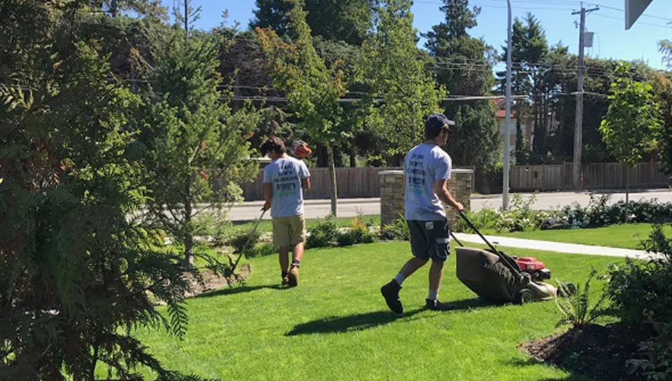 Two Atkinson Landscapers mowing and trimming a residential property front lawn