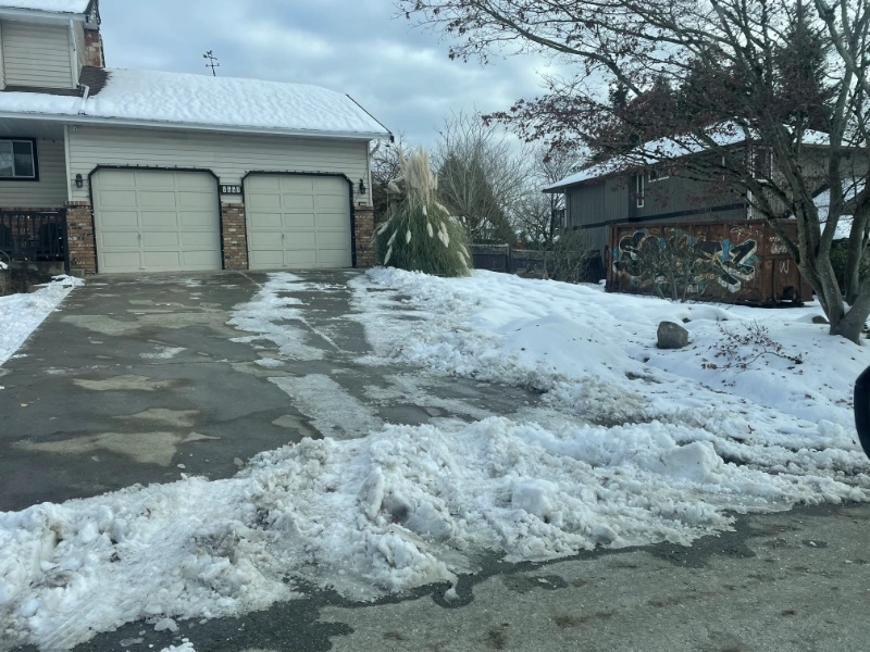 a snow covered yard with the driveway cleared of snow