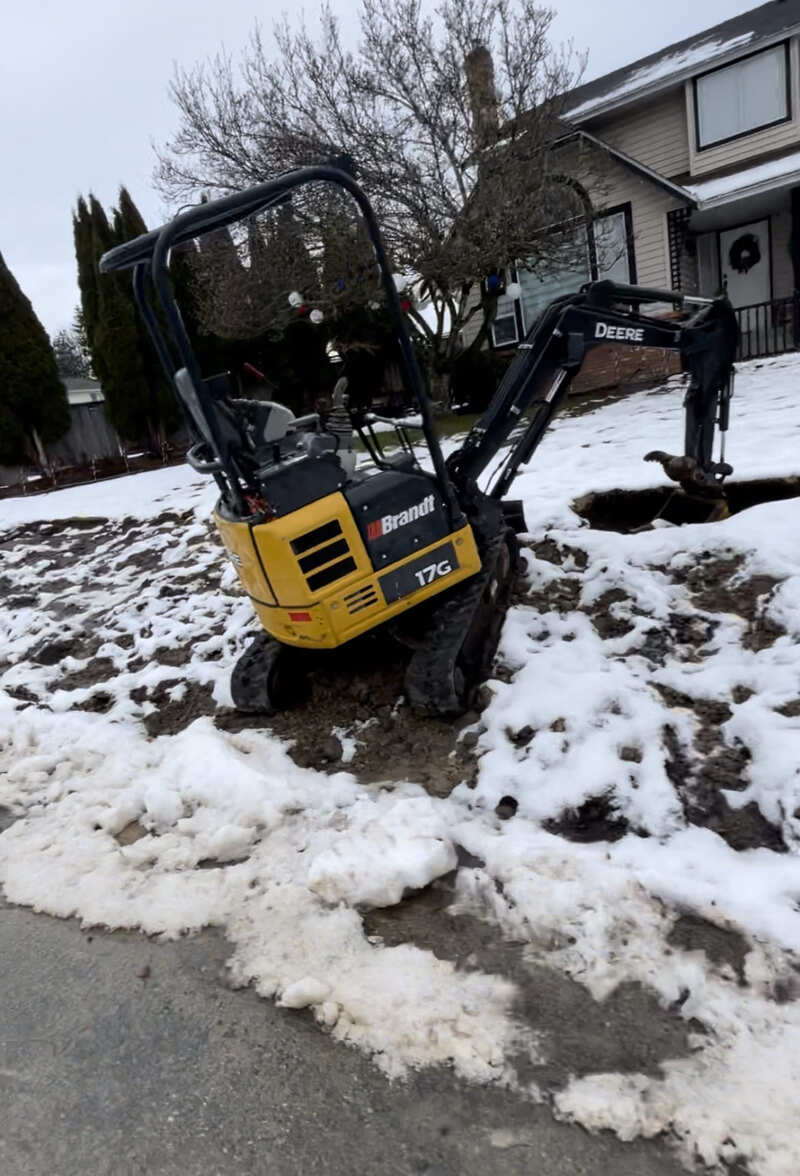 17g excavator parked on the front lawn in the snow with the bucket down