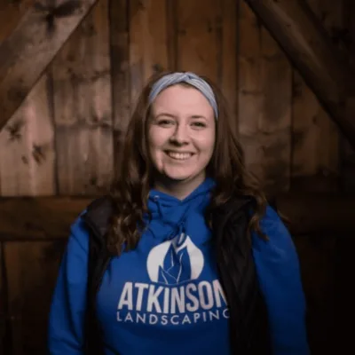 atkinsonlandscaping staff kaella in a blue atkinson hoodie against a wood background